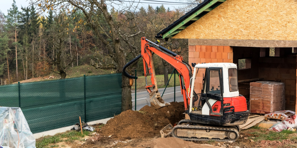 Residential Excavation Contractors at work with a backhoe working on moving earth on the side of a unfinished house.